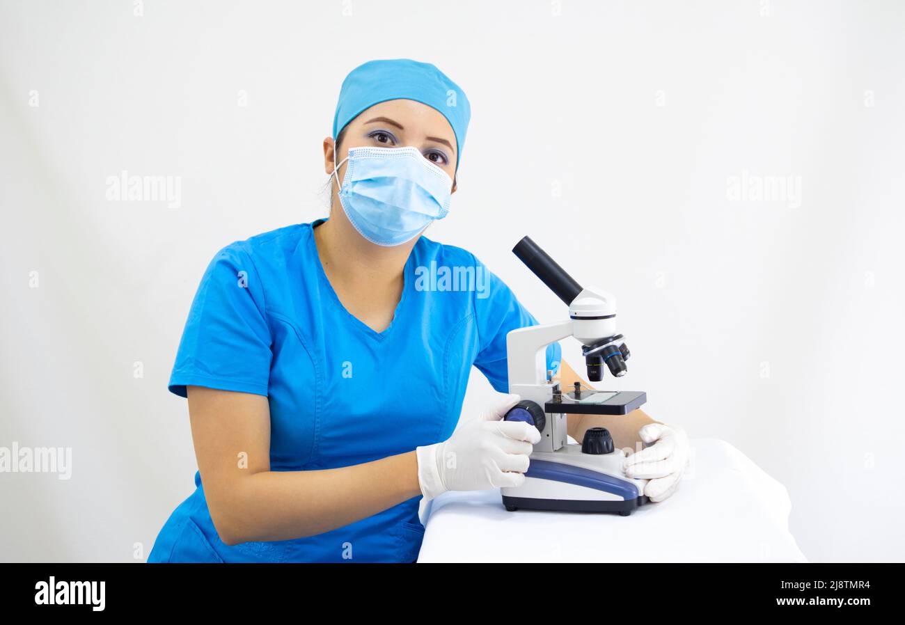 Schöne Frau Labortechniker trägt einheitliche und blaue OP-Kappe, chirurgischen Schutz, Analyse von Proben mit dem Mikroskop, auf weißem Hintergrund Stockfoto