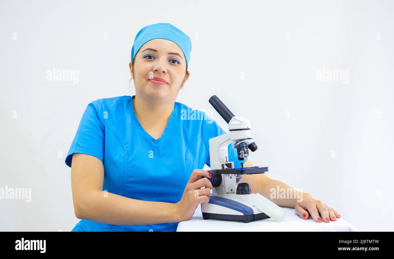 Schöne Frau Labortechniker trägt einheitliche und blaue OP-Kappe, Analyse der Proben mit dem Mikroskop, auf weißem Hintergrund Stockfoto