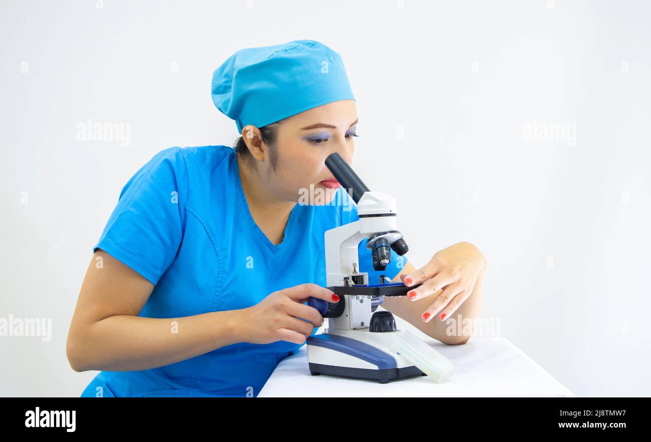 Schöne Frau Labortechniker trägt einheitliche und blaue OP-Kappe, Analyse der Proben mit dem Mikroskop, auf weißem Hintergrund Stockfoto