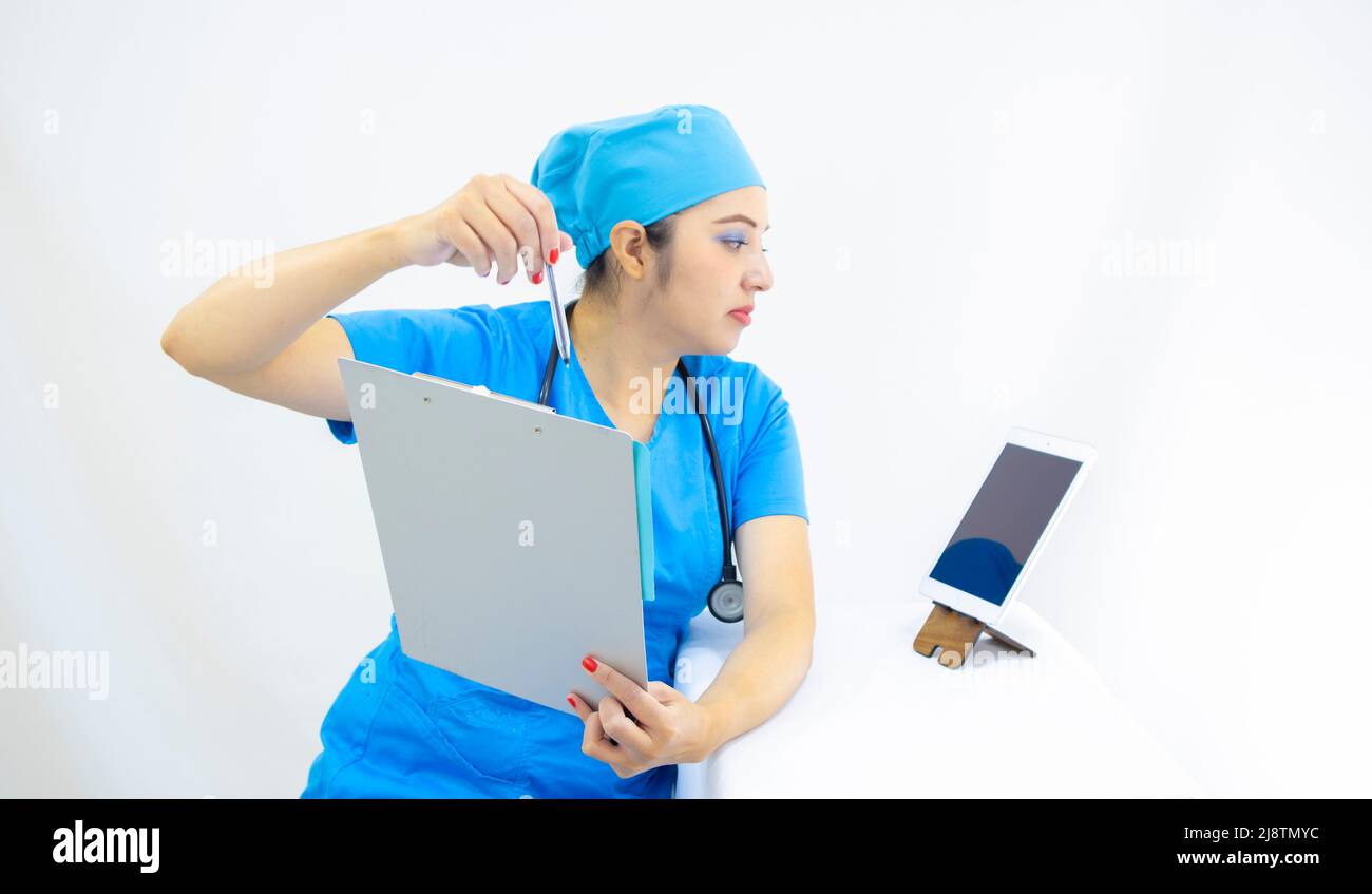 Schöne Ärztin, trägt blaue Uniform und blaue OP-Kappe, Stethoskop am Hals, mit der Tablette, um Ergebnisse zu zeigen, auf weißem Hintergrund Stockfoto