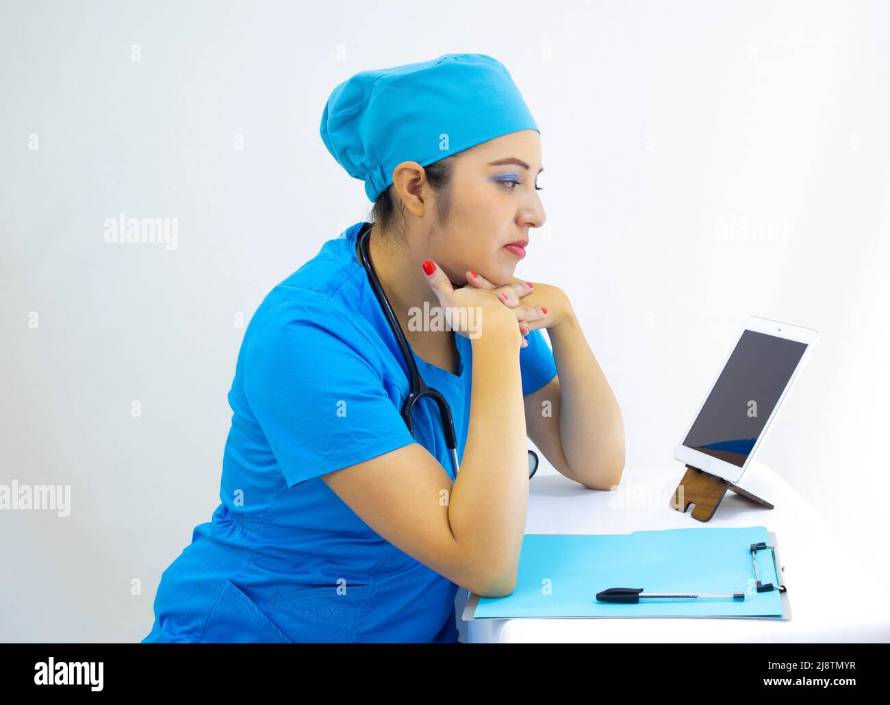 Schöne Frau Labortechnikerin trägt Uniform und blaue OP-Kappe, in Videoanruf, um Ergebnisse zu liefern, auf weißem Hintergrund Stockfoto