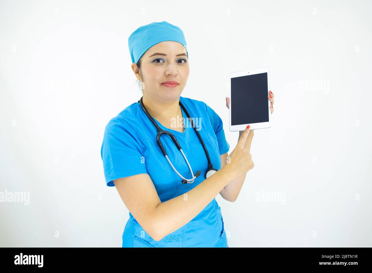 Schöne Ärztin, trägt blaue Uniform und blaue OP-Kappe, Stethoskop am Hals, mit dem Tablet, um die Ergebnisse auf weißem Hintergrund anzuzeigen Stockfoto