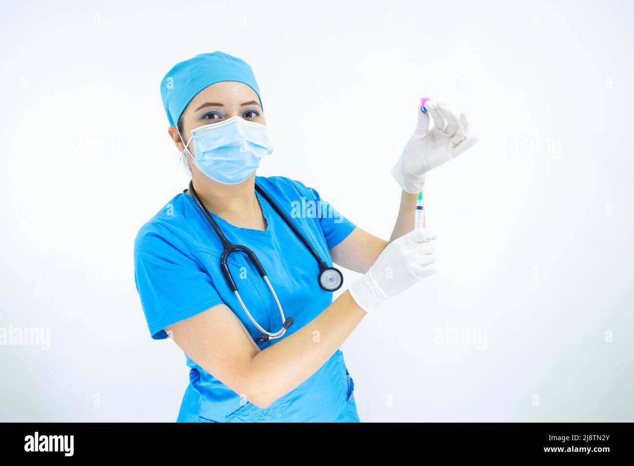 Schöne Frau Arzt trägt Maske Gesicht, einheitliche und blaue OP-Kappe, Stethoskop und Latexhandschuhe, Vorbereitung der Injektion auf weißem Hintergrund Stockfoto