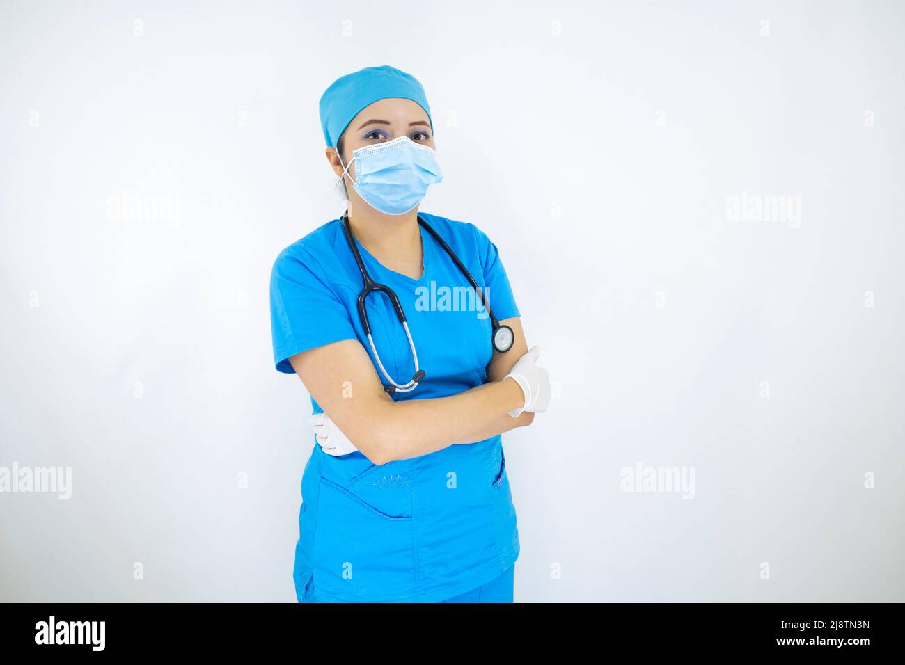 Schöne Ärztin trägt Uniform und blaue OP-Kappe, Gesichtsmaske und Latexhandschuhe. Professionelle Frau auf weißem Hintergrund Stockfoto