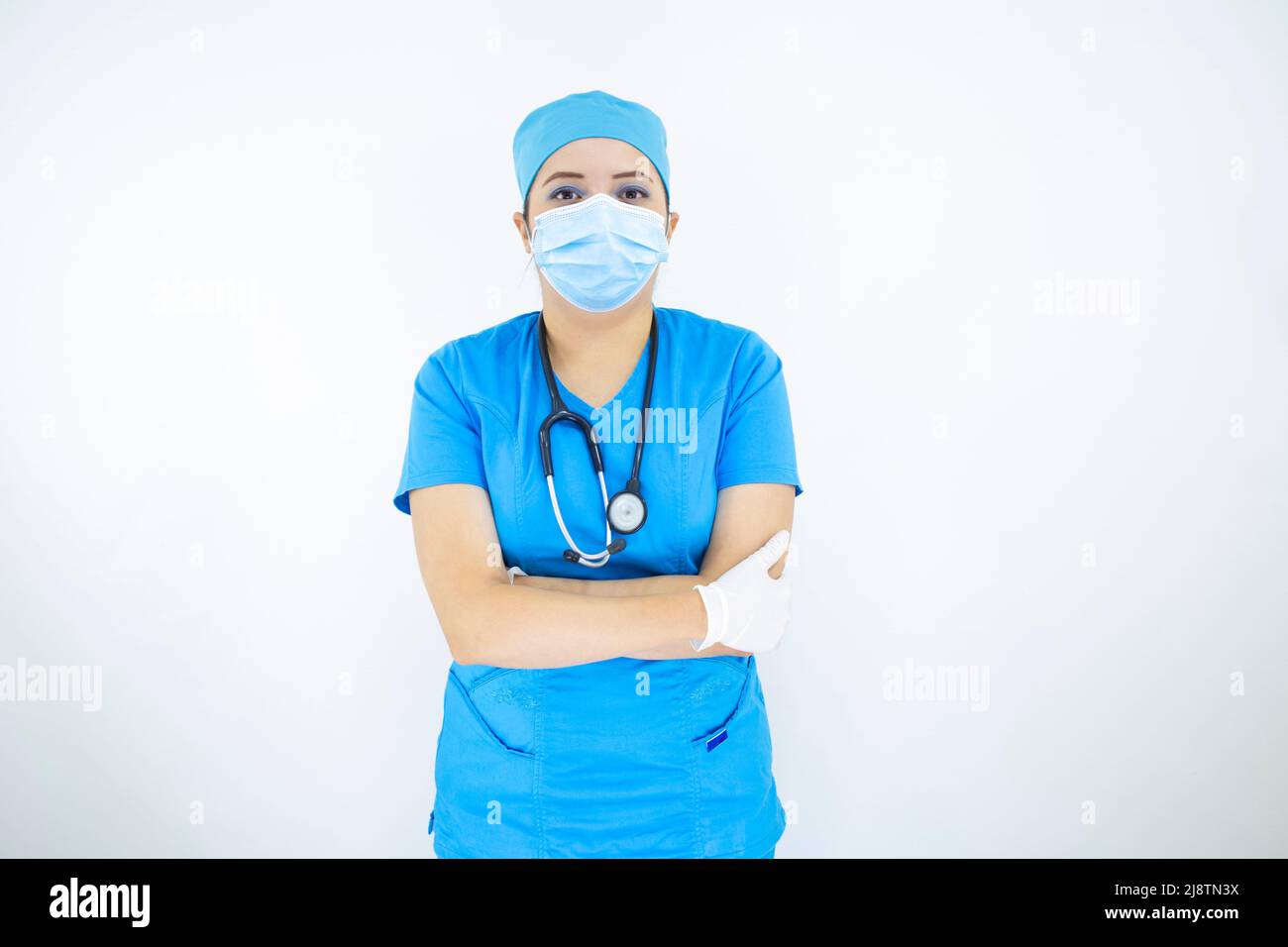Schöne Ärztin trägt Uniform und blaue OP-Kappe, Gesichtsmaske und Latexhandschuhe. Professionelle Frau auf weißem Hintergrund Stockfoto