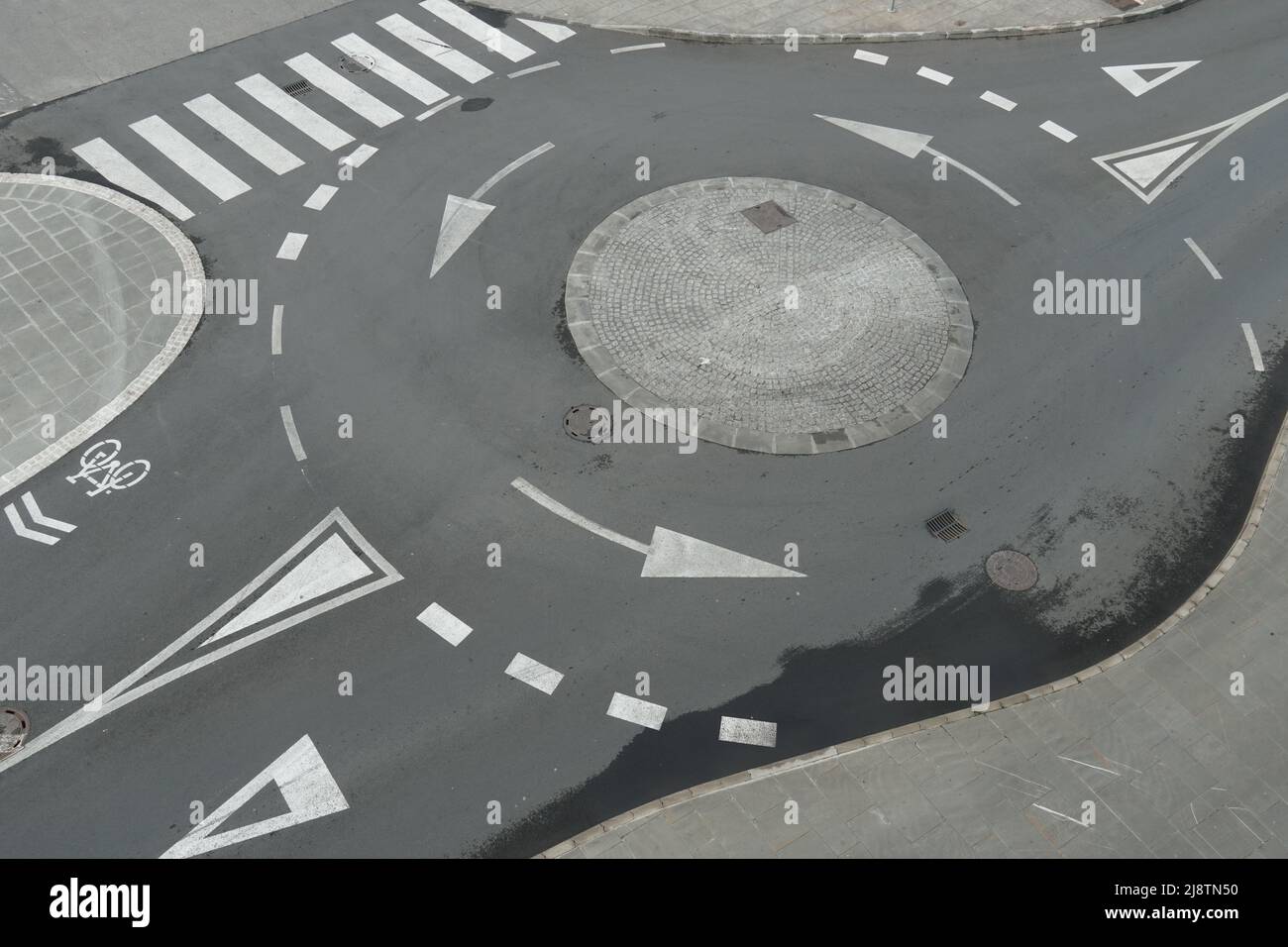 Luftaufnahme von oben auf einem leeren Kreisverkehr oder einer Kreisverkehr-Straße mit weißen Pfeilen, Fußgängerüberwegen und anderen Verkehrssignalen oder Markierungen in der europäischen Stadt. Stockfoto