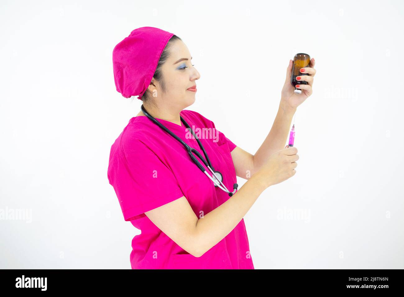 Schöne Frau medizinische Assistentin trägt Uniform und rosa OP-Kappe, Stethoskop, Vorbereitung der Injektion auf weißem Hintergrund Stockfoto