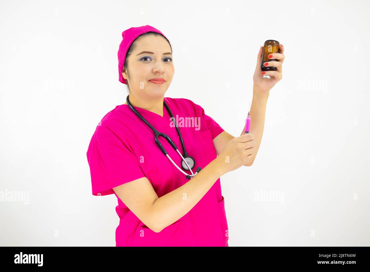 Schöne Frau medizinische Assistentin trägt Uniform und rosa OP-Kappe, Stethoskop, Vorbereitung der Injektion auf weißem Hintergrund Stockfoto