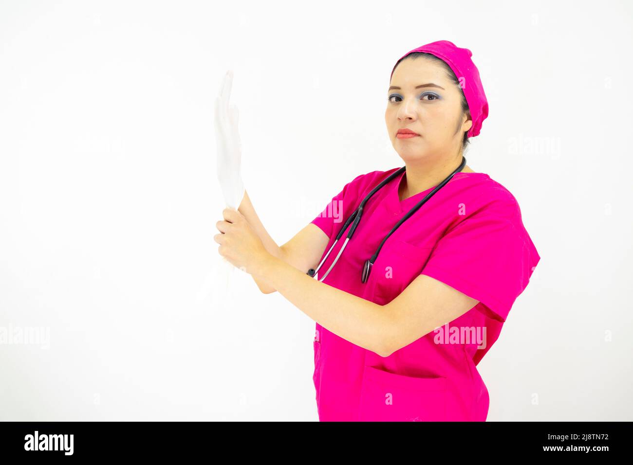 Schöne weibliche medizinische Assistentin trägt Uniform und rosa OP-Kappe, Stethoskop, Putting Latexhandschuhe, auf weißem Hintergrund Stockfoto