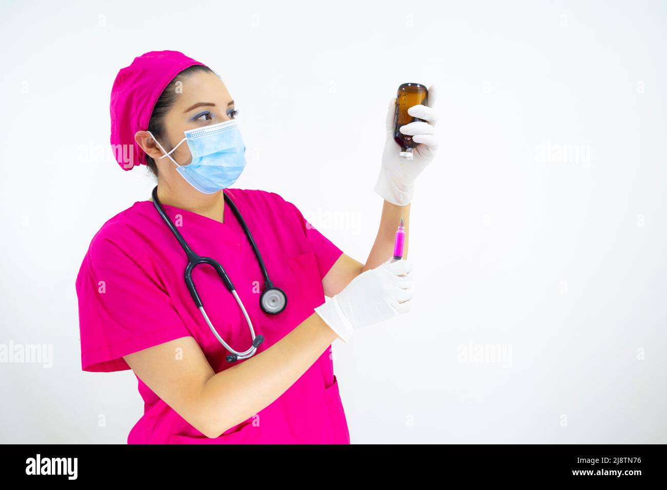 Schöne Frau medizinische Assistentin trägt Uniform und rosa OP-Kappe, Stethoskop und Latexhandschuhe, Vorbereitung der Injektion auf weißem Hintergrund Stockfoto