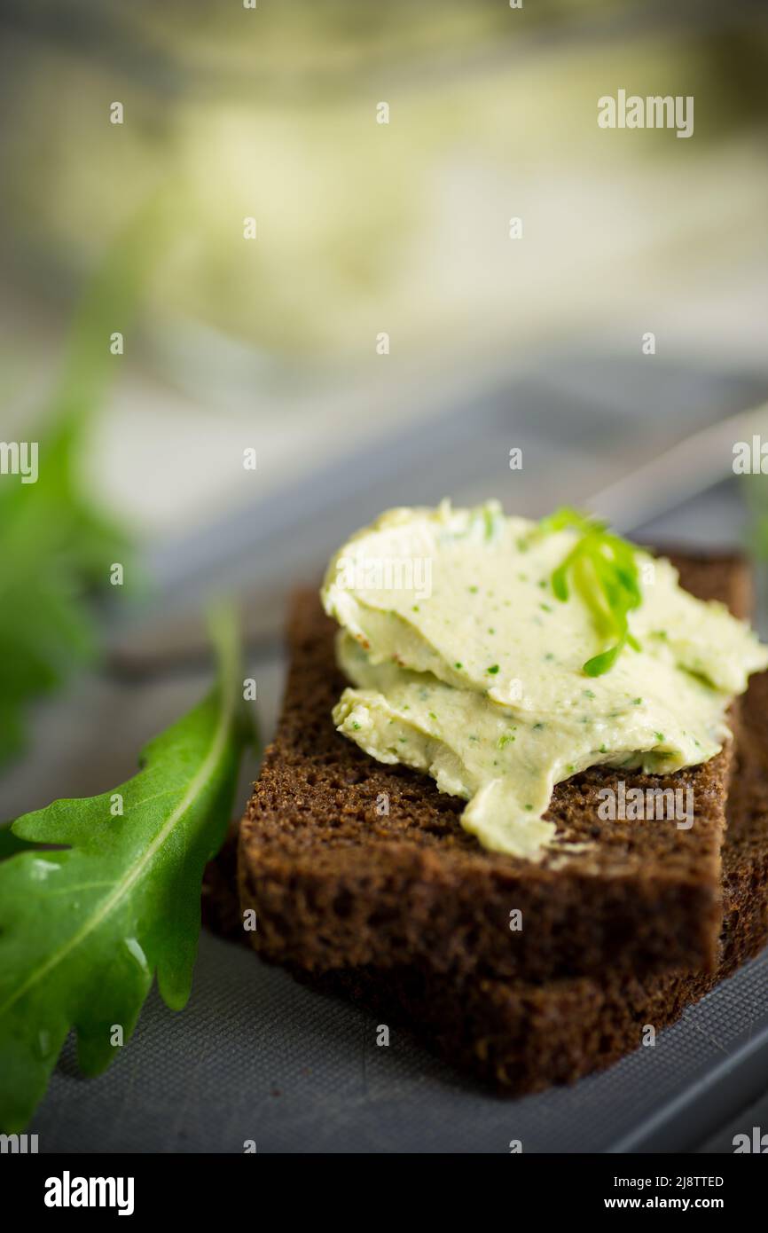 Brotkäse mit Knoblauch und Rucola auf dunklem Brot, auf einem Holztisch. Stockfoto