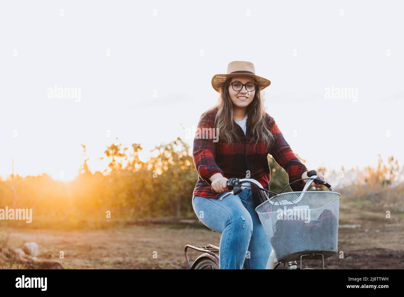Die lateinische Bäuerin reitet auf einem Oldtimer-Fahrrad mitten auf ihrem Ackerland. Nachhaltiger Verkehr. Stockfoto