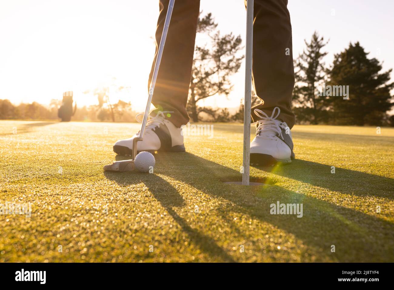 Niedriger Abschnitt eines kaukasischen jungen Mannes mit Schläger, Ball und flagstick in einem Loch auf dem Golfplatz Stockfoto