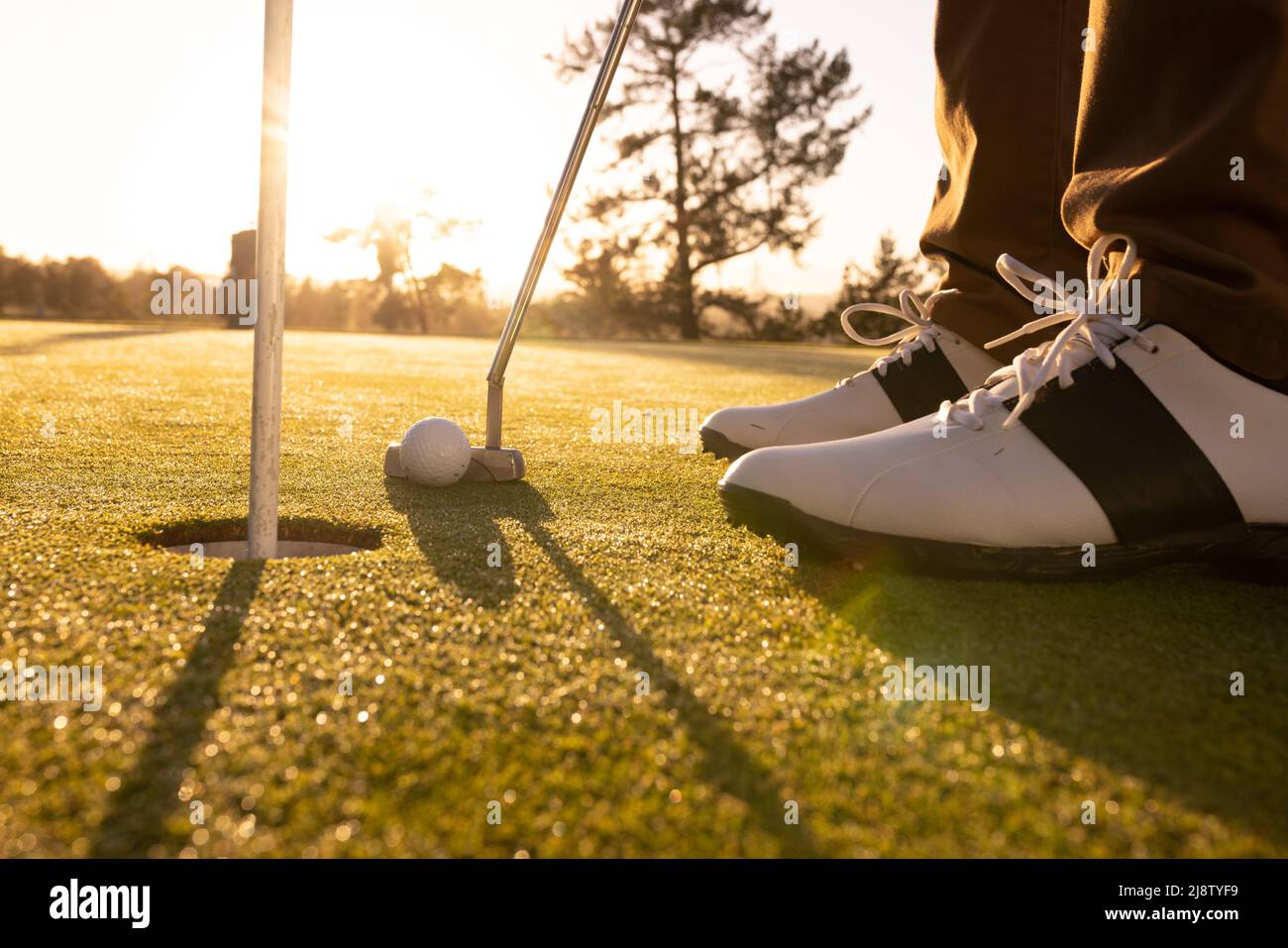 Unterer Abschnitt eines kaukasischen jungen Mannes mit Ball, Schläger und flagstick in einem Loch auf dem Golfplatz Stockfoto