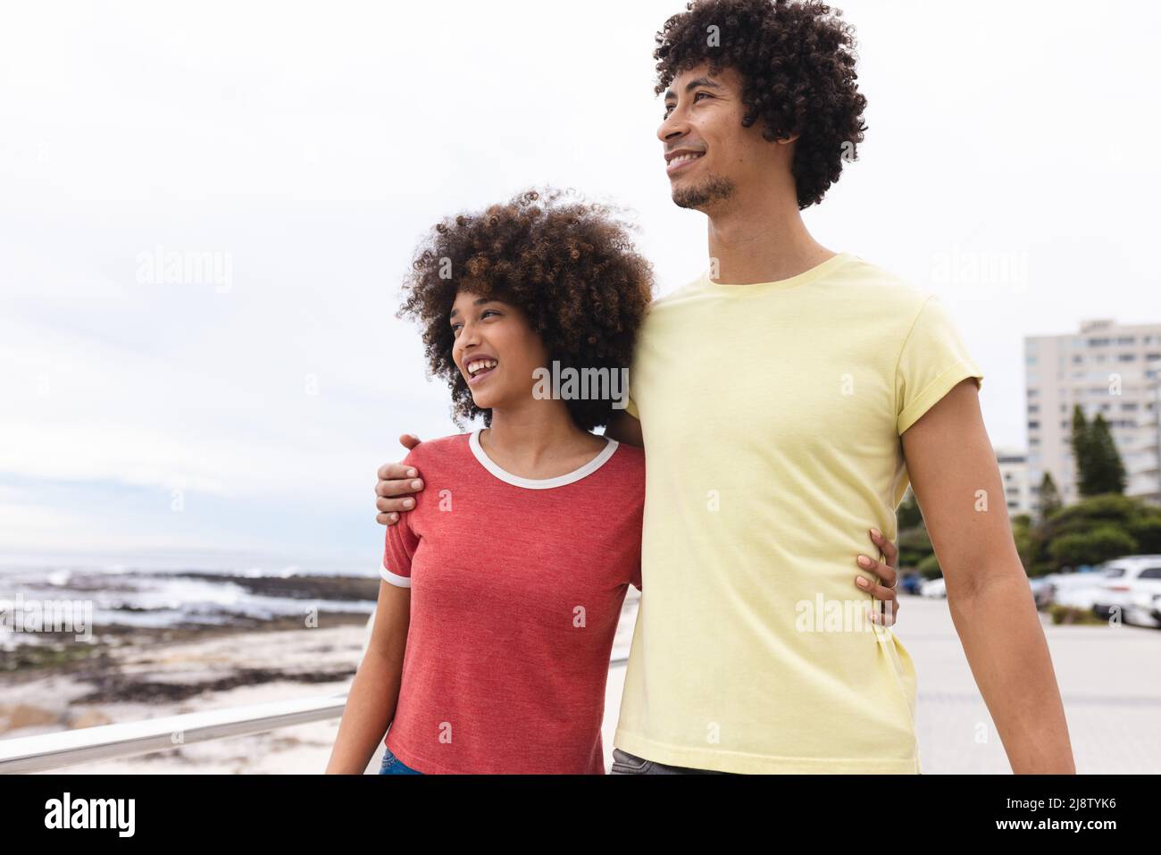 Lächelndes, junges afro-afroamerikanisches Paar, das wegschaut, während es gegen den Himmel steht und Raum kopiert Stockfoto