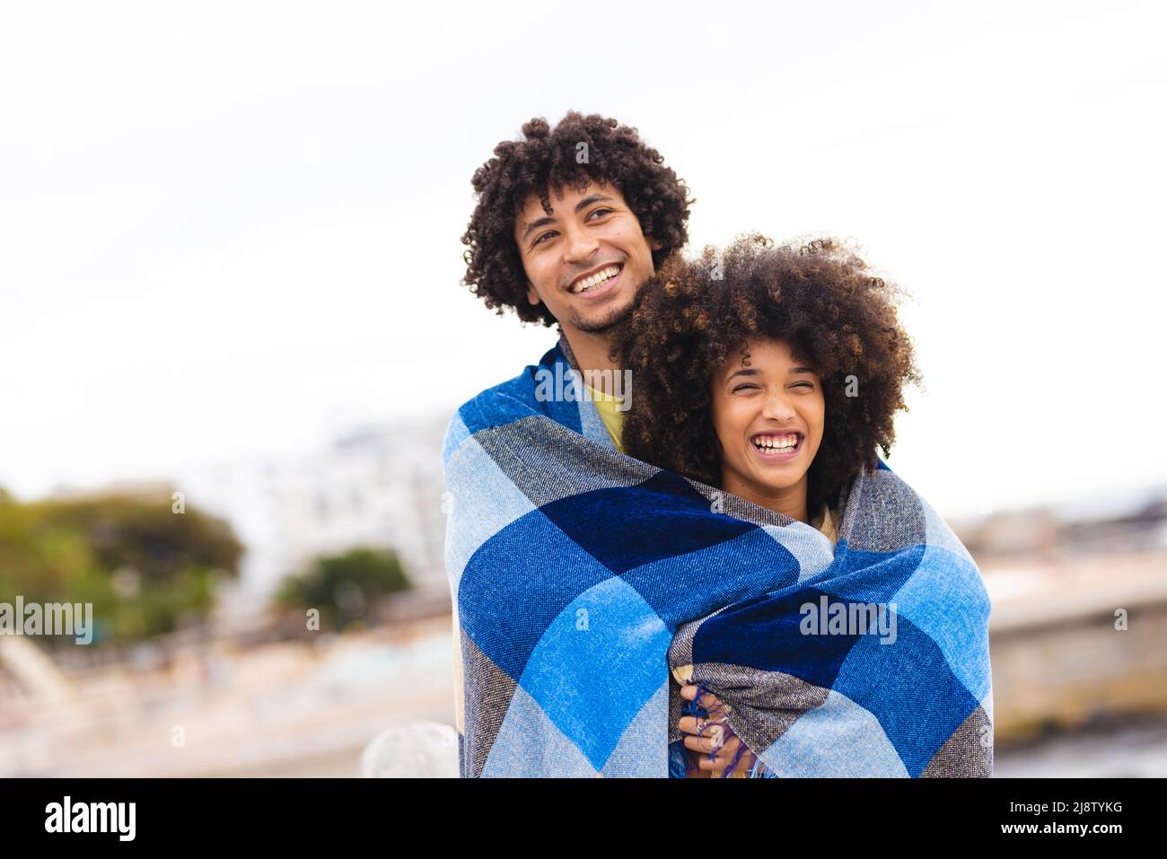 Fröhliches junges afro-afroamerikanisches Paar unter blauer Decke gegen den Himmel gewickelt, Raum kopieren Stockfoto