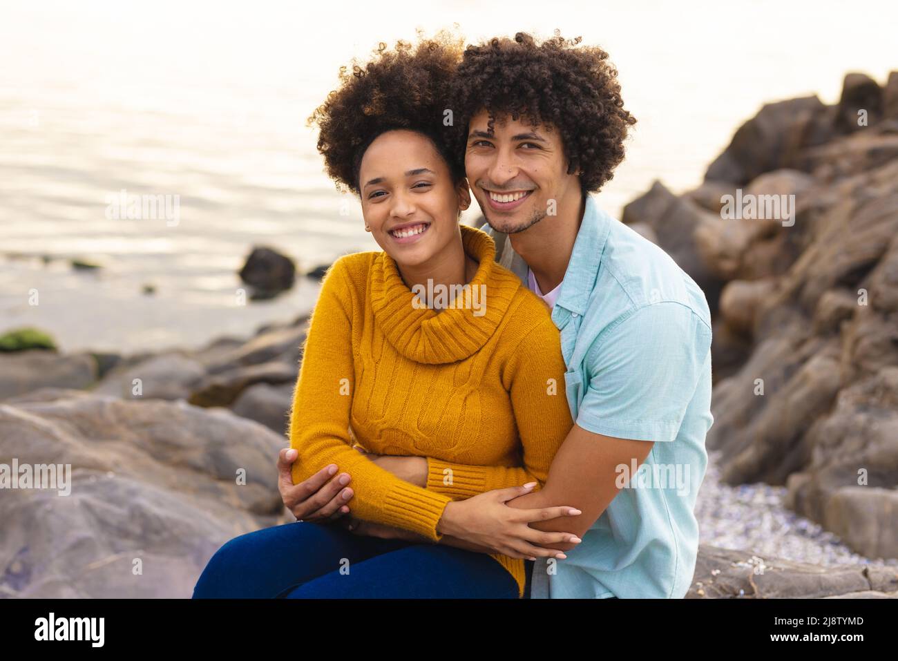 Porträt eines lächelnden afro-amerikanischen jungen Paares, das am Strand sitzt Stockfoto