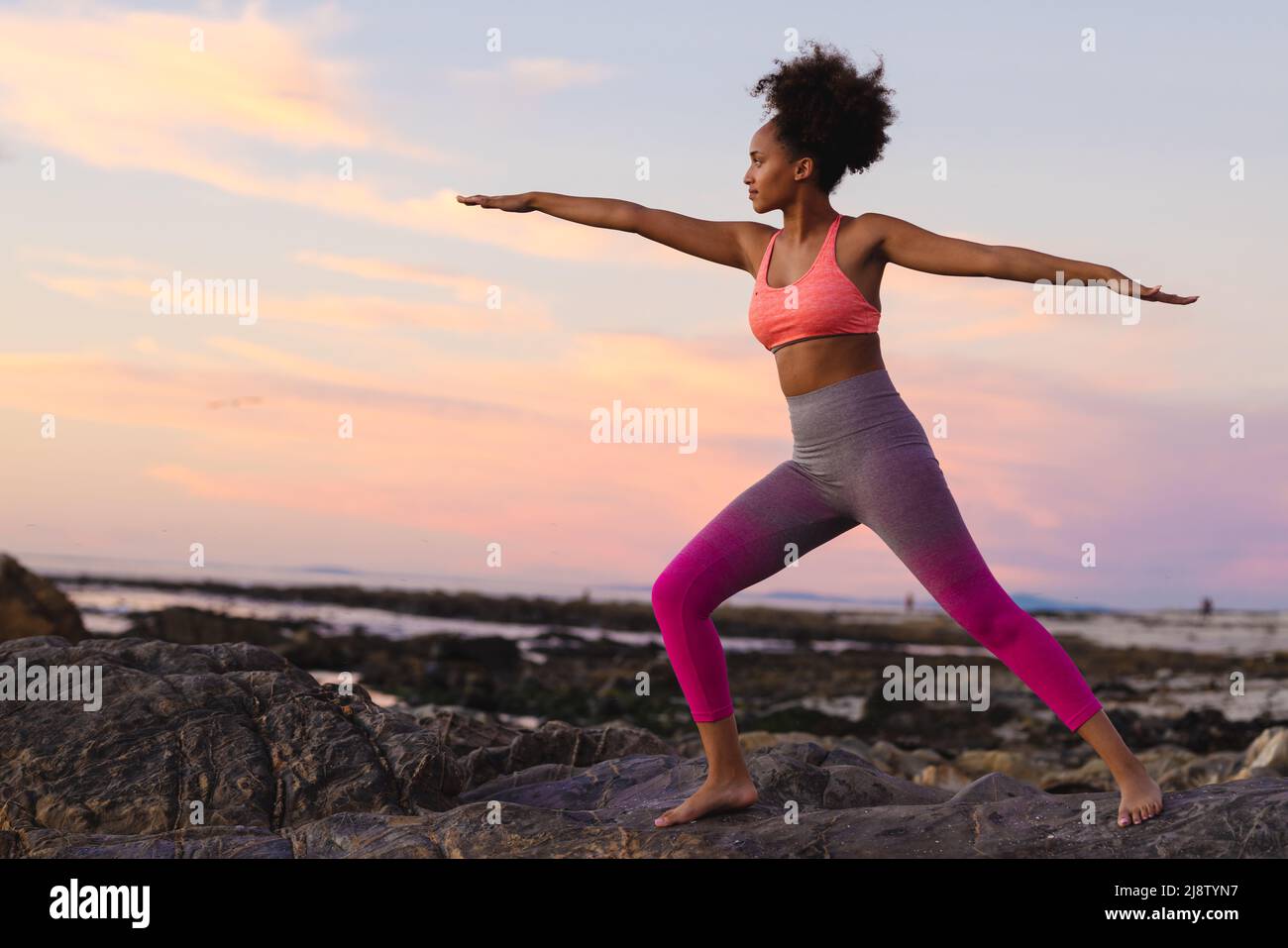 Junge afro-afroamerikanische Frau mit ausgestreckten Armen beim Training am Strand während des Sonnenuntergangs Stockfoto