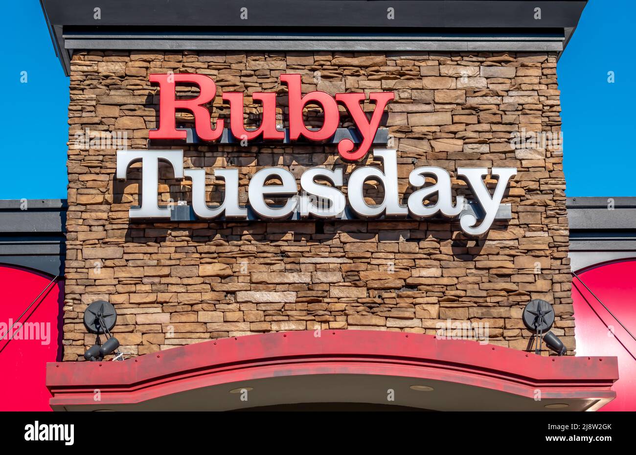 Außenwerbung mit „Ruby Tuesday“-Marke und Logo für den Außenbereich in kräftigen rot-weißen Buchstaben vor einem Steinhintergrund an einem hellen, sonnigen Tag. Stockfoto