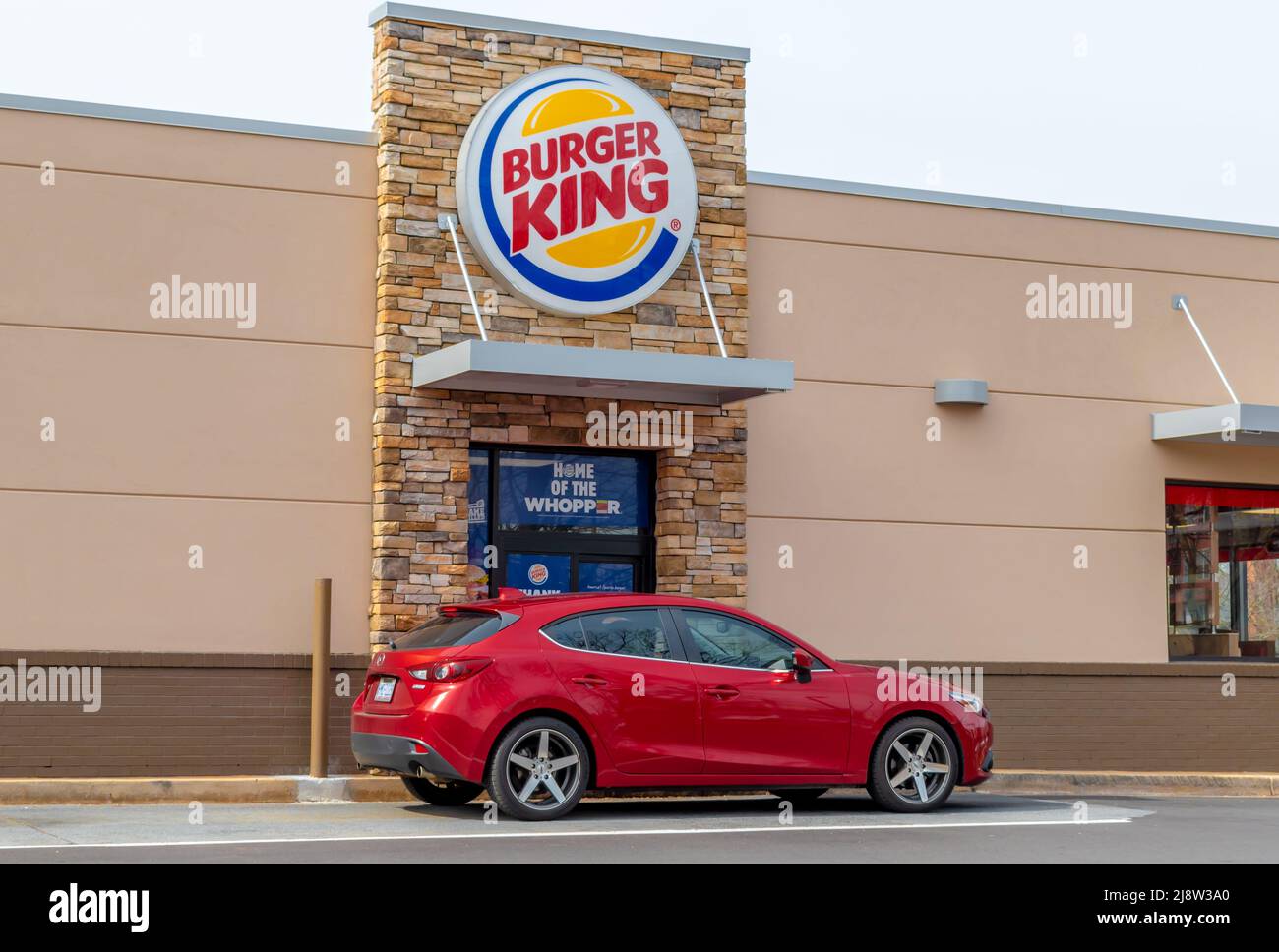 Außenwerbung, Fassadenmarke und Logo für „Burger King“ an seinem Drive-Thru-Fenster im sanften Licht des frühen Morgens an einem sonnigen Tag mit einem roten Fahrzeug. Stockfoto