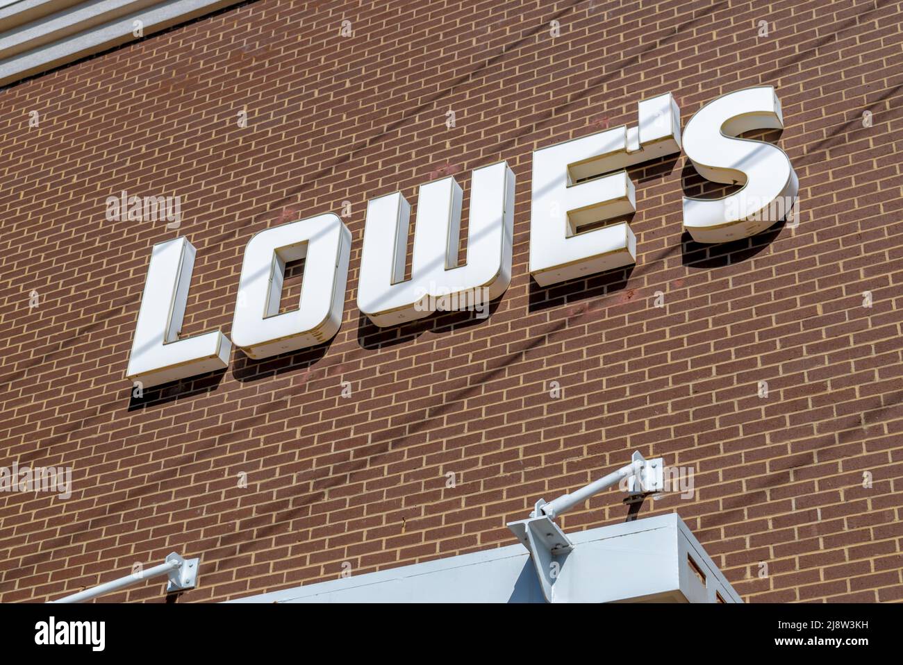 Außenwerbung mit „Lowes“-Marke und Logo in dreidimensionalen, weißen Buchstaben vor braunem Backsteingebäude in hellem Sonnenlicht. Stockfoto