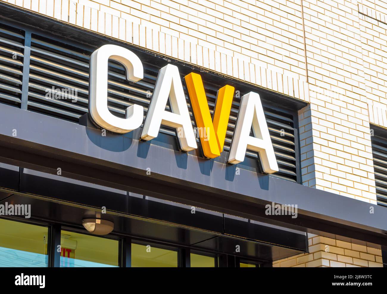 Außenfassade mit Marken- und Logo-Beschilderung für das Restaurant „CAVA“ im mediterranen Stil in großen weißen und gelben Buchstaben über Glasfenstern an einem sonnigen Tag. Stockfoto