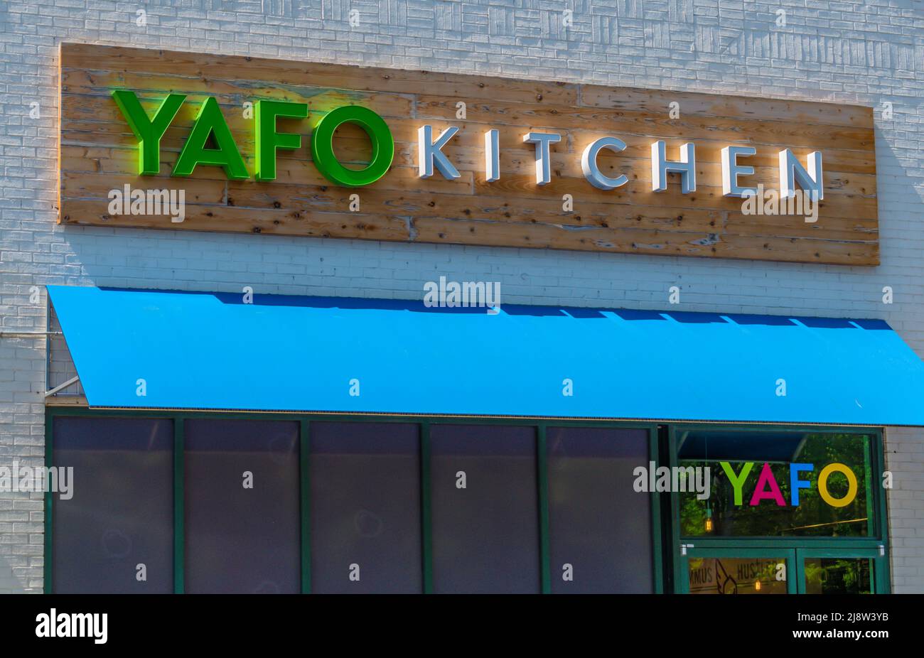 Außenfassade der Marke „YAFO Kitchen“ und Logo-Beschilderung in grünen und weißen Buchstaben über leuchtendem blauen Markise und Glasfenstern an einem hellen sonnigen Tag. Stockfoto