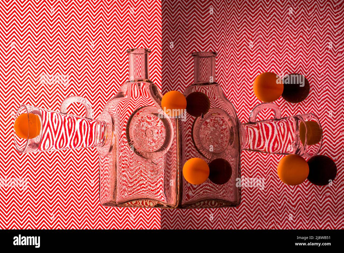 Abstraktes Stillleben mit Glaswaren und Kugeln auf einem roten geometrischen Hintergrund Stockfoto