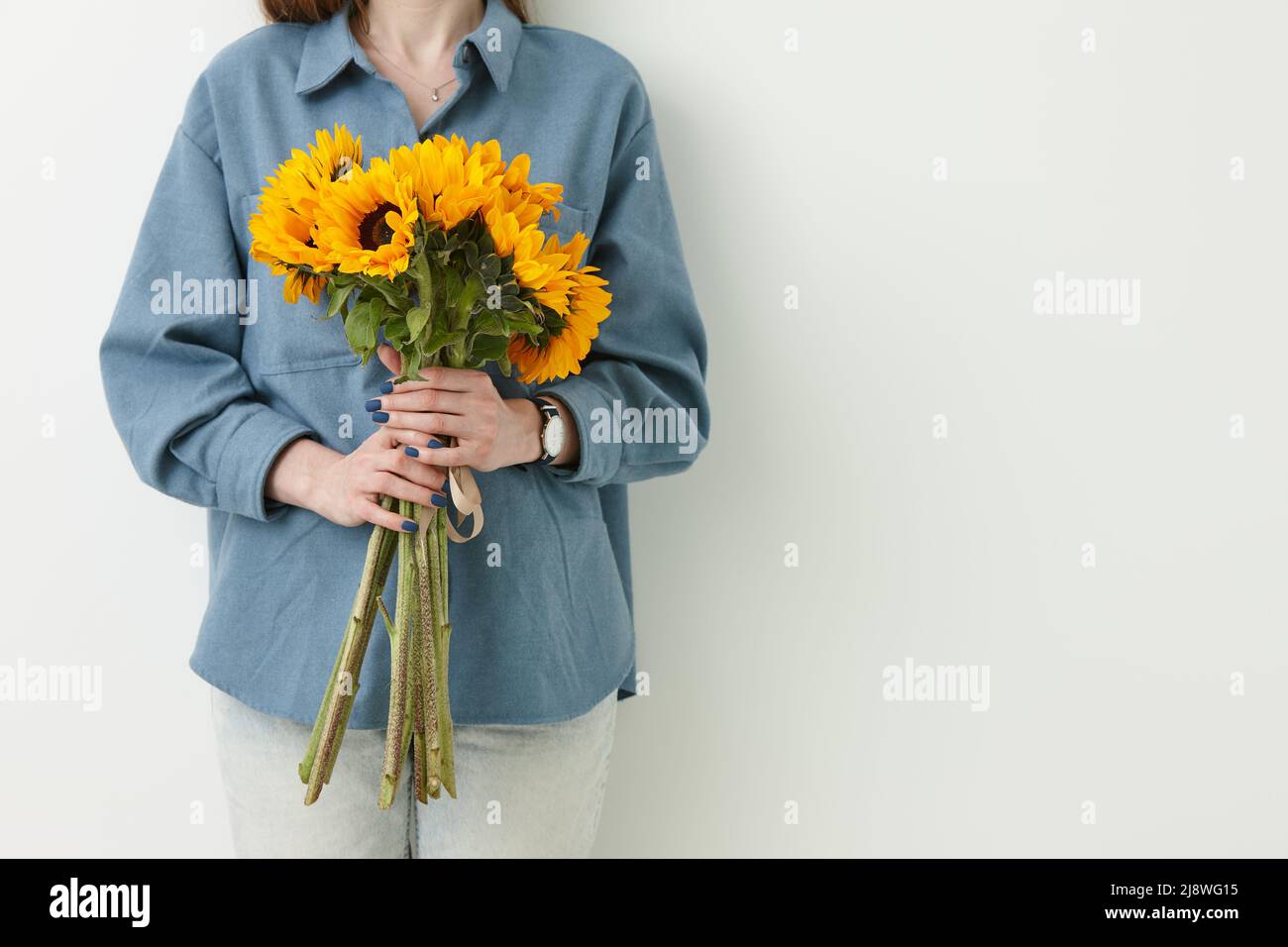 Ukrainische Frau mit einem Haufen Sonnenblumen auf weißem Wandhintergrund Stockfoto