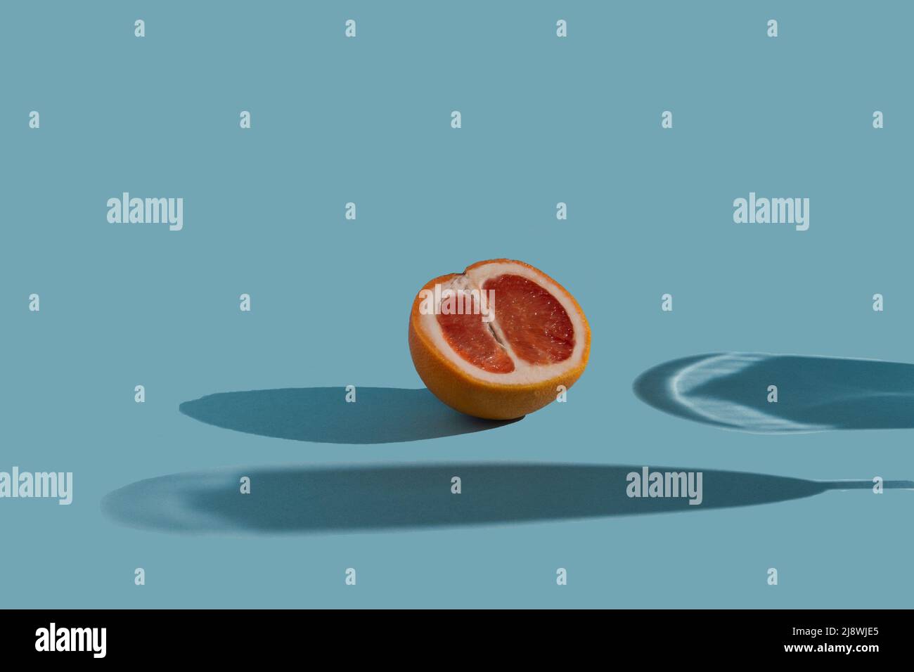 Rote Grapefruit und Glasschatten auf blauem Untergrund. Minimales Konzept mit scharfen Schatten. Trendige soziale Mockup oder Tapete Stockfoto