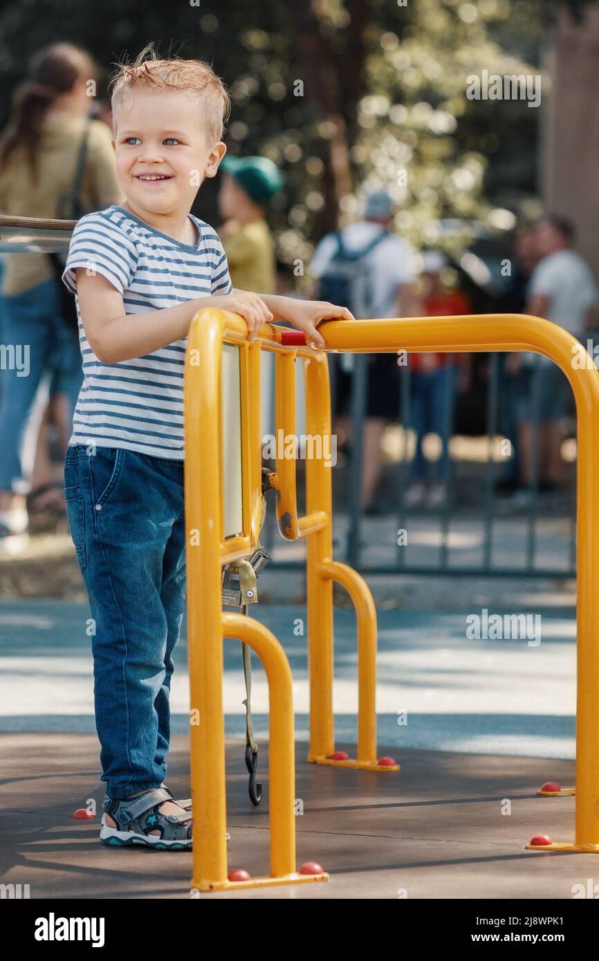 Kleiner Junge, der sich auf einem Spielplatz im Freien auf dem Karussell im Kreisverkehr amüsieren kann. Stockfoto