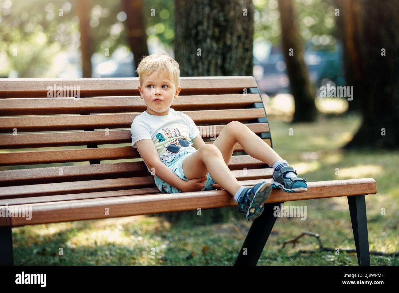 Netter Junge, der auf einer Bank im Park sitzt und sich ausruhen kann. Stockfoto