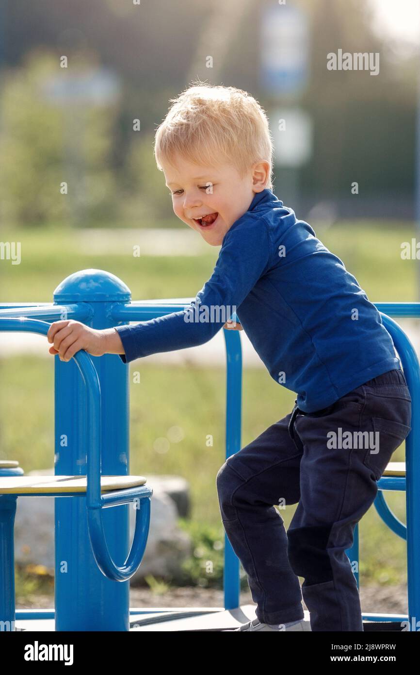 Kind im Karussell. Junge dreht sich auf dem Karussell für Kinder auf dem Spielplatz. Junior Schuljunge spielt allein. Kind in blauem Pullover mit blonden Haaren. Guy ist es Stockfoto