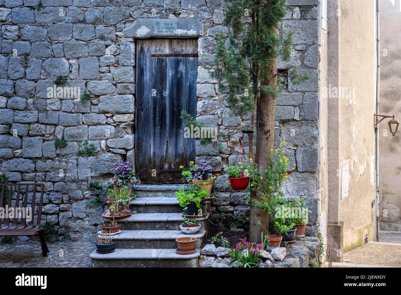 Alte schwarze Holztür in einer Steinmauer mit Stufen und Blumentöpfen Stockfoto