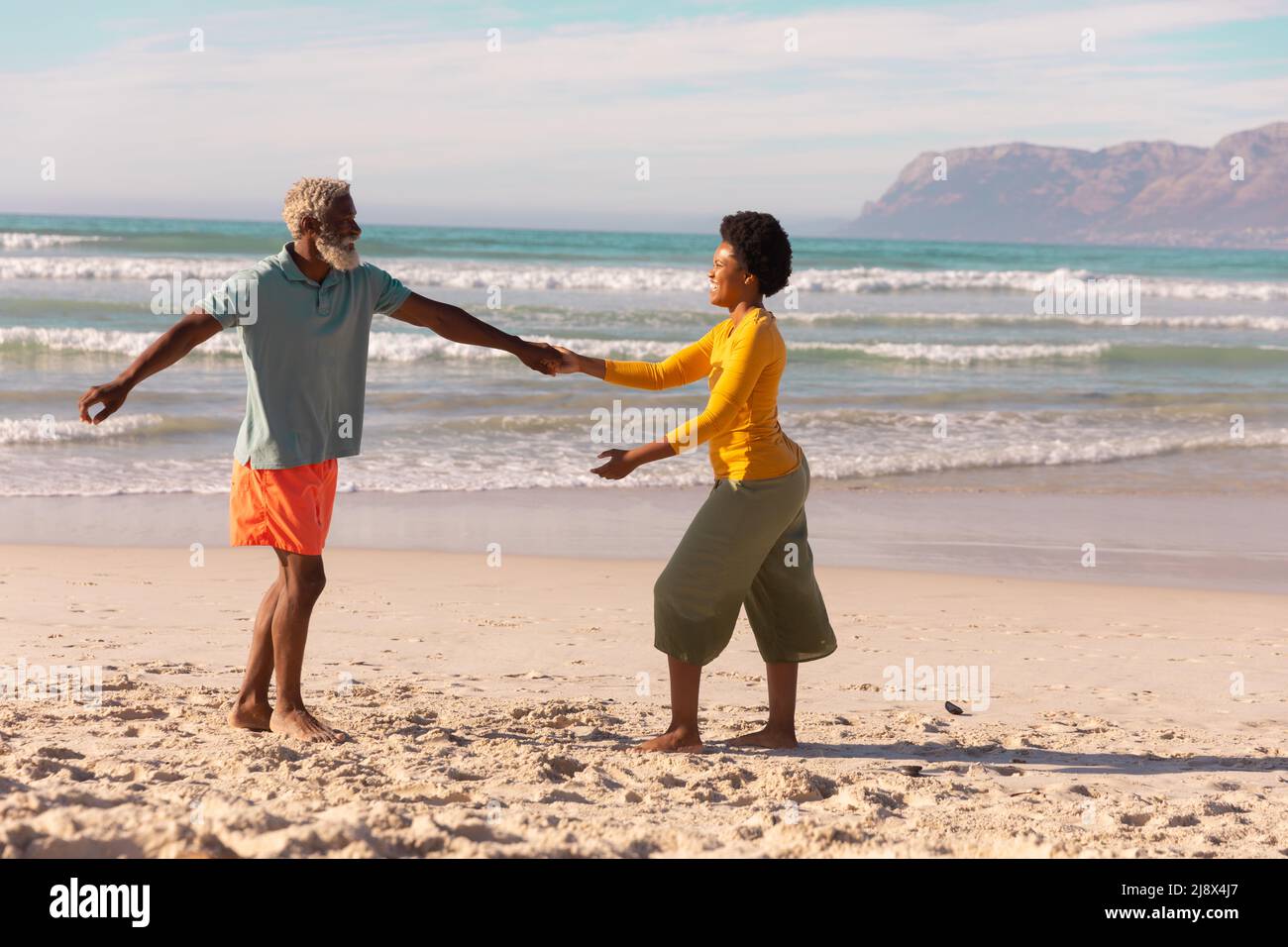 Bärtiger afroamerikanischer Senioren, der im Sommer mit einer reifen Frau gegen Meer und Himmel tanzt Stockfoto