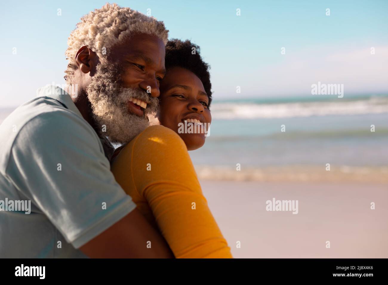 Seitenansicht eines glücklichen bärtigen afroamerikanischen Senioren, der eine reife Frau gegen Meer und Himmel umarmt Stockfoto