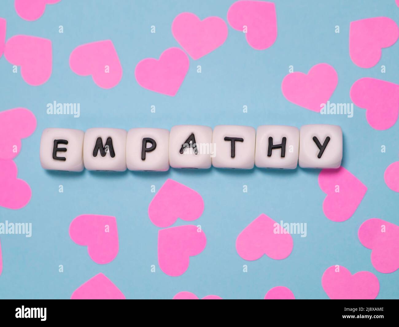 Das Wort „Einfühlungsvermögen“ wurde mit weißen Perlen auf blauem Hintergrund mit rosa Herzen präsentiert. Stockfoto