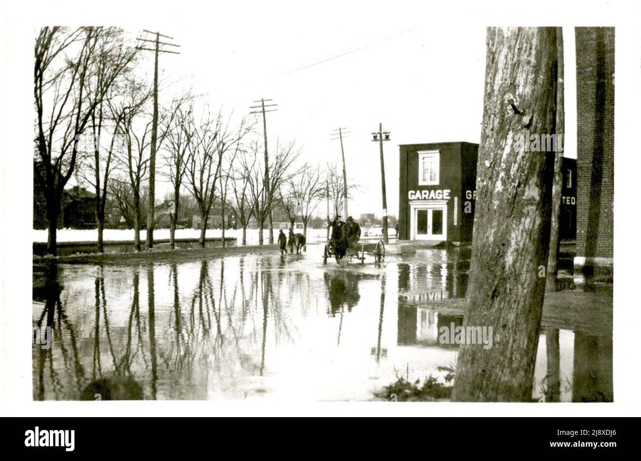 Ein Pferd und ein Wagen und ein Mann, der ein Pferd während der Flut von 1918 in Greenleaf's Garage auf der Station and Foundry Street in Belleville, Ontario, durch das Flutwasser führt. Der Fluss Moira neben der Station Street ist mit Eis bedeckt Stockfoto