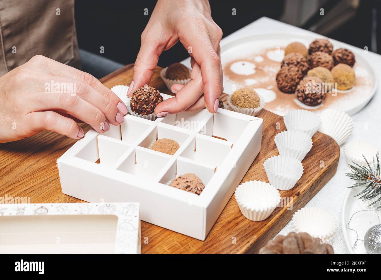 Hochwertige handgefertigte Schokoladentrüffel. Eine Konditorin verpackt Schokolade in Schachteln. Nahaufnahme von weiblichen Händen und leckeren Süßigkeiten. Weibliche Hände. Stockfoto