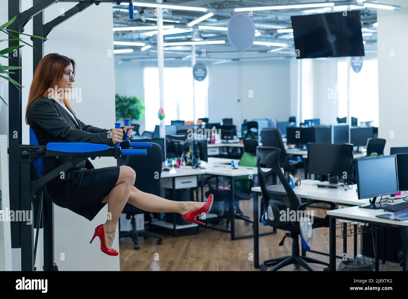 Geschäftsfrau macht Übungen an der montierten horizontalen Bar im Büro. Sport während einer Arbeitspause. Stockfoto