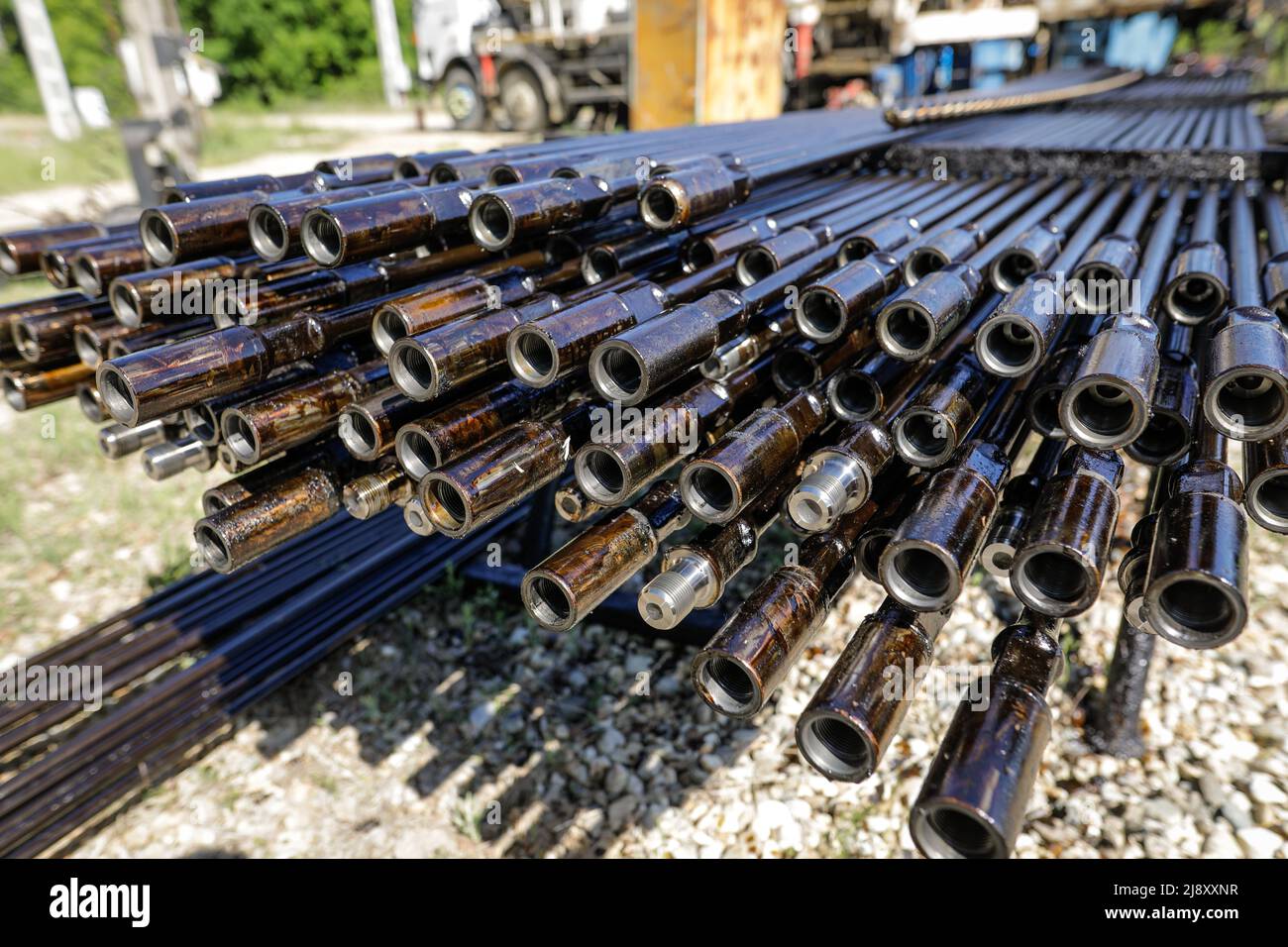 Bohrrohre für Ölbohranlagen, die im Hintergrund mit Mitarbeitern der Ölindustrie gestapelt sind. Öl- und Gasindustrie. Ölpumpe Wagenheber auf einem Ölfeld. Bohren von Öl und Stockfoto