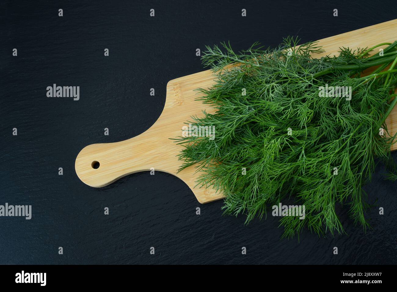 Haufen Dill oder Fenchel auf einem hölzernen Schneidebrett auf schwarzem Hintergrund, Draufsicht. Aromatische Würze Stockfoto