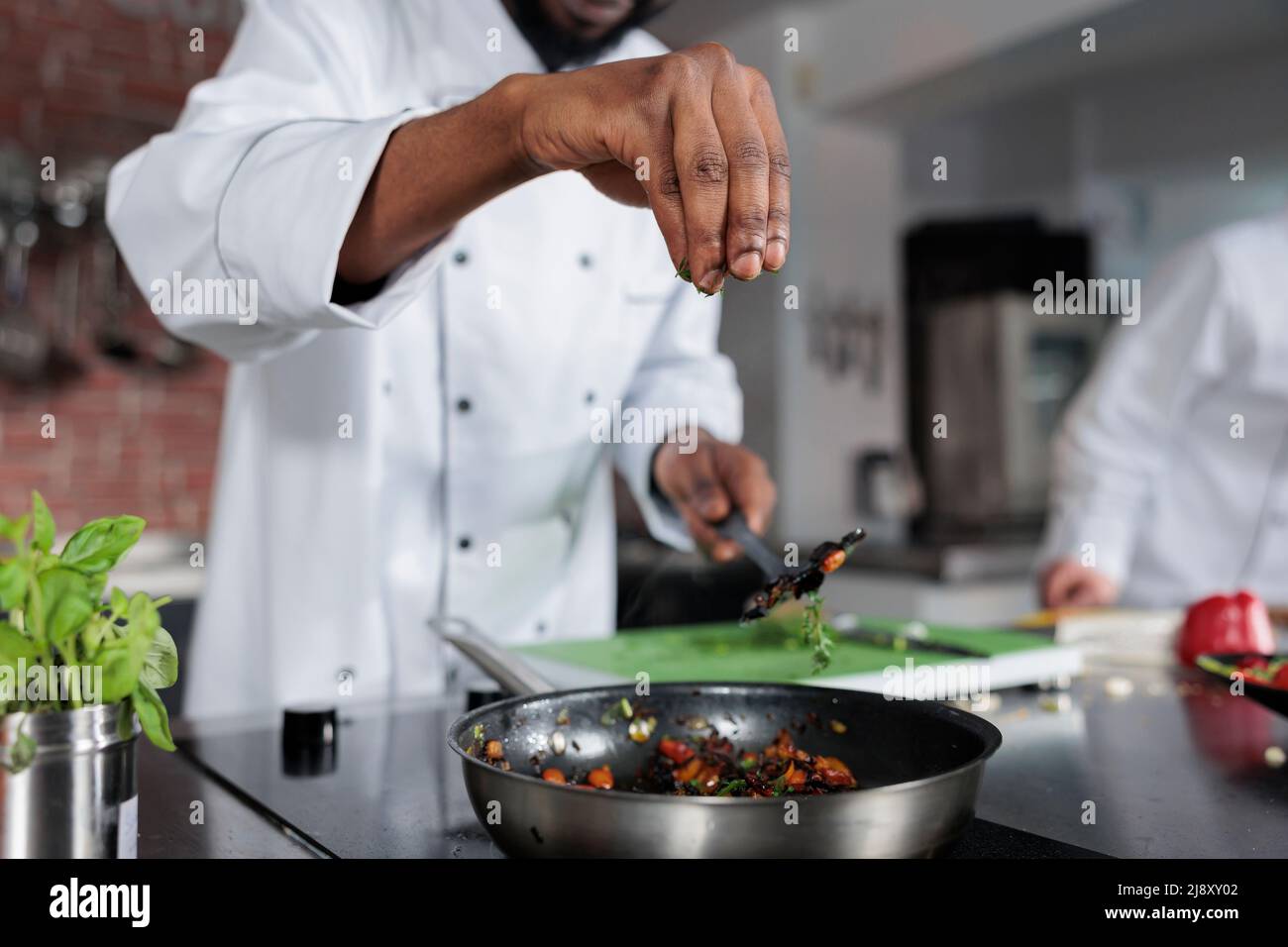 Hauptkoch würzt Gericht für Essen Wettbewerb im feinen Restaurant vorbereitet. Kopf kochen werfen frische gehackte Kräuter in der Pfanne, um den Geschmack der Mahlzeit zu verbessern, während in der professionellen Küche. Stockfoto