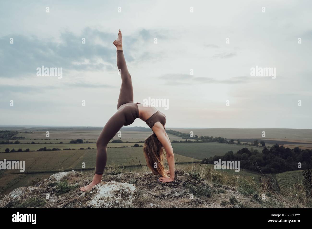 Junge Frau macht Gymnastik-Übungen auf einem Hügel im Freien, schöne Landschaft auf dem Hintergrund Stockfoto