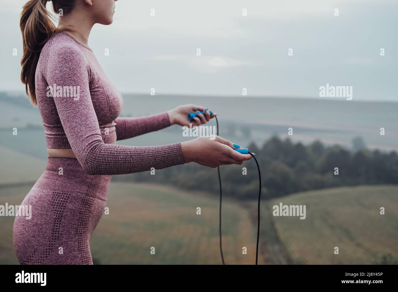 Seitenansicht einer nicht erkennbaren jungen Frau, die das Springseil hält, Mädchen, die draußen auf dem Hügel arbeiten Stockfoto