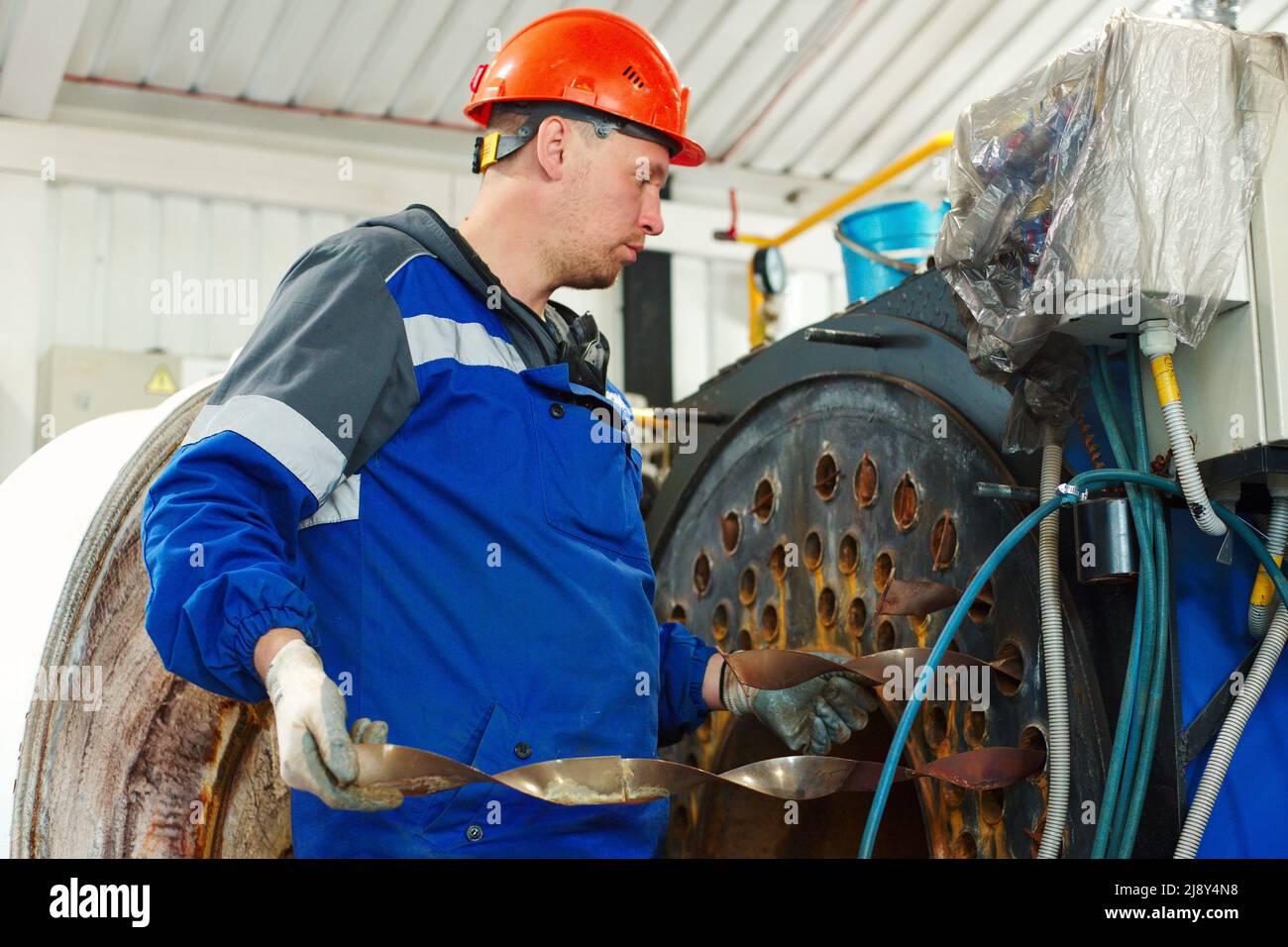 Ein Helmingenieur inspiziert und repariert die Gasanlagen im Kesselraum. Reinigung und Wartung des industriellen Dampfkessels. Stockfoto