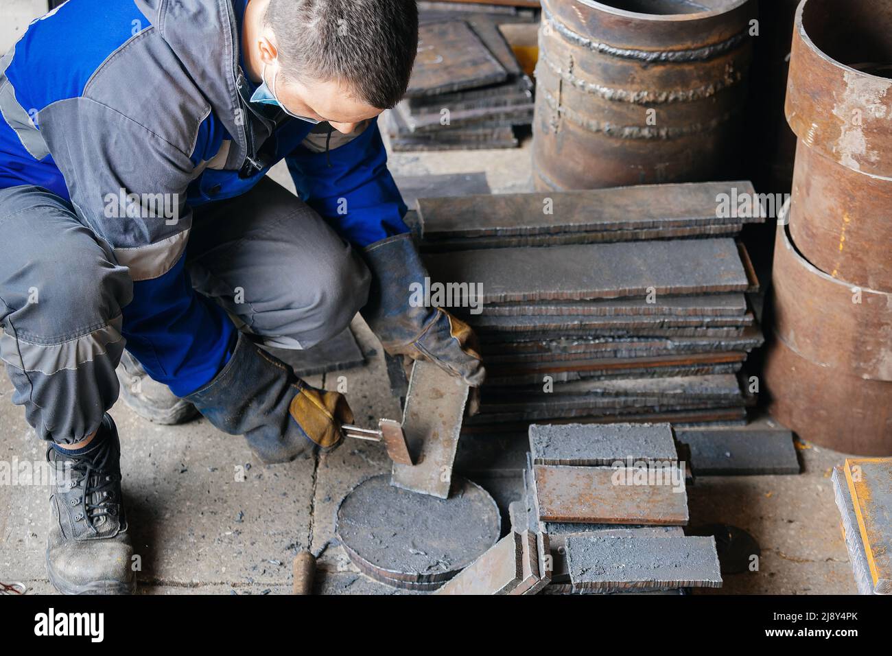 Arbeiter in der Schwerindustrie oder Metallurgie schlagen Eisenplatten mit Hammer ab. Arbeiten Sie mit Metall. Beschaffung von Wertstoffen für die Produktion. Authentischer Workflow. Stockfoto