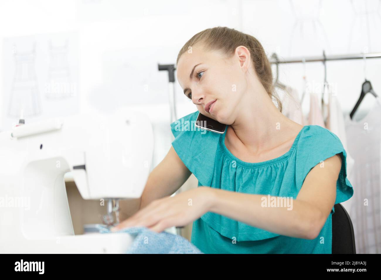 Frau auf der Nähmaschine, während sie am Telefon sprach Stockfoto