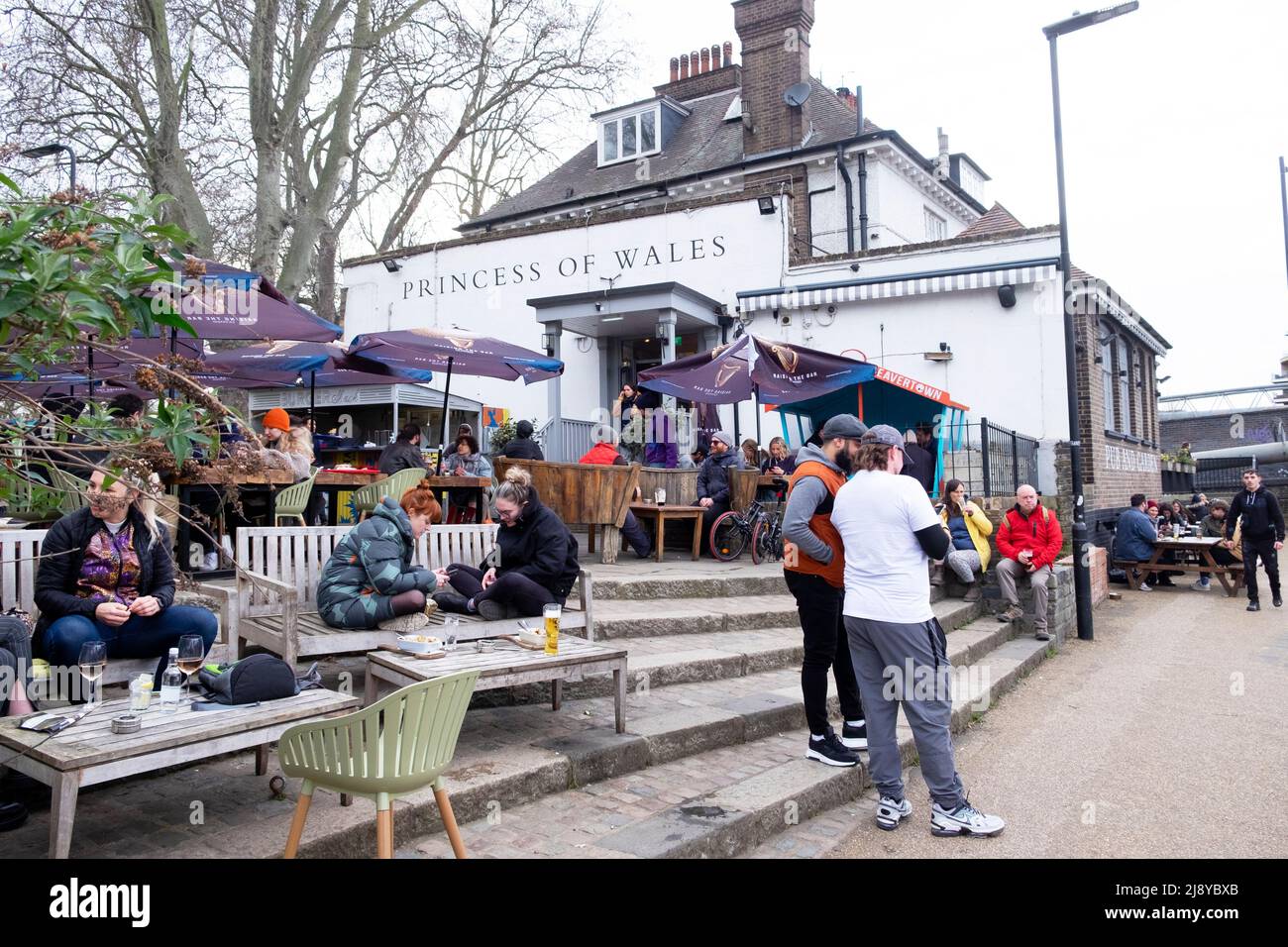 Menschen sitzen entspannt trinken und stehen vor dem Princess of Wales Pub im Frühjahr auf dem Fluss Lea Clapton London E5 England Großbritannien KATHY DEWITT Stockfoto