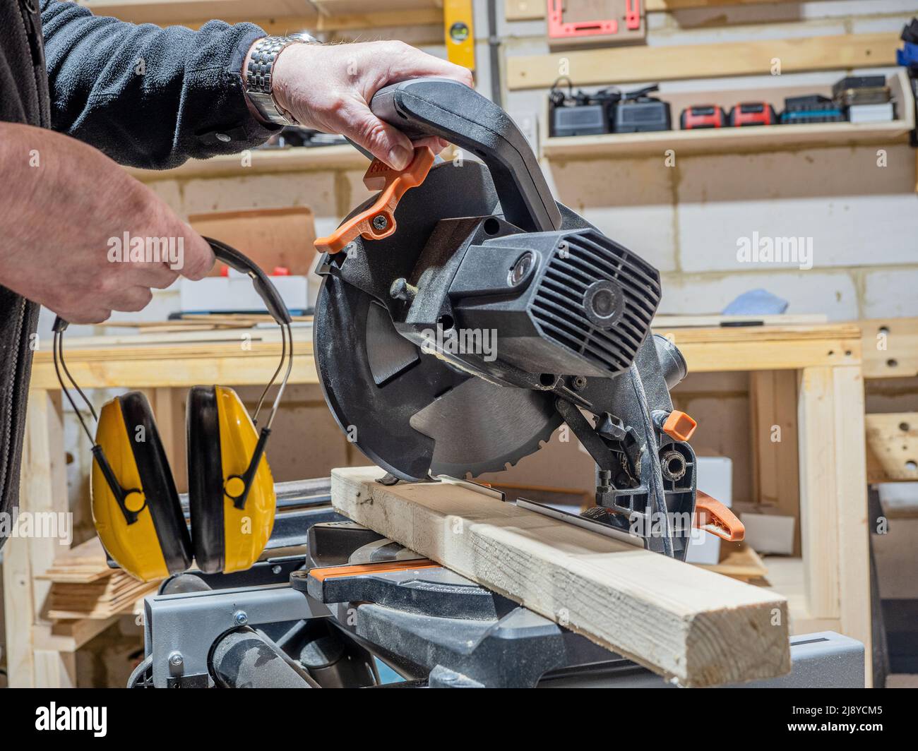 Handwerker, der sich bereit gemacht hat, eine elektrische Gehrungsäge mit gelben Ohrschützern zu verwenden Stockfoto